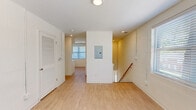 Located at 1100 E Washington Ave in East Point, Georgia, this two-story, 2-bedroom, 1-bathroom unit offers a practical and well-appointed layout. Entry is made through a ground-level foyer with painted cinder block walls and a tiled staircase with a wood handrail leading up to the main living level. The upper floor encompasses the majority of the living space and is finished with light wood laminate flooring throughout, creating a bright and cohesive feel.

The kitchen is a standout feature, outfitted with crisp white shaker-style cabinetry, black hardware accents, light countertops, and a full suite of stainless steel appliances including a gas range, microwave, dishwasher, and refrigerator. A large window fills the kitchen with natural light. The open hallway area includes an electrical panel and louvered closet door, providing practical storage access.

Both bedrooms feature painted cinder block walls, light wood flooring, and ceiling fans with integrated lighting. The primary bedroom is a comfortable size and benefits from natural light through a window with blinds. The bathroom is cleanly finished with white subway tile in the tub/shower surround, mosaic tile flooring, a white vanity with a single sink, and matte black fixtures throughout.