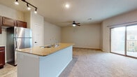 This single-story residence is designed around an open-concept layout that seamlessly connects the kitchen and living area. The kitchen is a standout feature, outfitted with rich, dark-toned cabinetry, granite countertops, a subway tile backsplash, and a full suite of stainless steel appliances including a refrigerator, electric range, and over-the-range microwave. A central island with a granite surface and an integrated sink adds both workspace and a natural division between the kitchen and the expansive carpeted living area. Track lighting illuminates the kitchen, while a ceiling fan serves the living space, contributing to a comfortable and functional atmosphere throughout.

The bedrooms are generously proportioned, each finished with plush wall-to-wall carpet, neutral-toned walls, and ceiling fans. Windows fitted with blinds allow natural light to filter in while maintaining privacy. The bathroom features wood-look tile flooring, a full soaking tub with a tiled surround, a toilet, and a vanity with granite countertops complemented by dark wood cabinetry. The overall color palette throughout the unit is neutral and cohesive, with warm beige tones creating a calm, move-in-ready ambiance across all spaces.