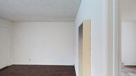 This single-floor space presents a straightforward and functional interior defined by its clean, minimalist aesthetic. The walls are finished in crisp white, creating a bright and open atmosphere that allows for versatile use of the space. Underfoot, rich dark hardwood-style flooring adds warmth and contrast against the light walls, grounding the interior with a classic, practical finish. The ceiling features a textured popcorn finish, a detail that adds subtle depth to the otherwise smooth surfaces throughout. A prominent built-in HVAC wall unit is positioned along one wall, indicating dedicated climate control for year-round comfort. The overall layout is open and unobstructed, providing a blank canvas well-suited for a variety of configurations. The space is compact yet functional, with clean lines and neutral finishes that make it adaptable to different uses or furnishing styles. The combination of white walls, dark flooring, and the textured ceiling gives the interior a no-frills, utilitarian character that prioritizes practicality and ease of maintenance.