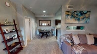 Located at 1240 Enclave Cir in Arlington, Texas, this single-story residence offers a thoughtfully arranged layout with a warm, neutral palette throughout. The living room serves as a central gathering space, highlighted by a classic brick fireplace and direct access to an outdoor patio through double French doors that invite natural light into the room. Vaulted ceiling angles add a sense of vertical openness, and ceiling fans are present to enhance comfort.

The living area flows naturally into a dedicated dining space, defined by plush carpeting and anchored by a framed wall mirror that adds depth to the room. A pass-through opening connects the dining area to the kitchen, maintaining a sense of openness between the spaces. The galley-style kitchen is well-appointed with dark espresso cabinetry, granite-look countertops, wood-look vinyl flooring, and black appliances including a range and refrigerator, along with a dishwasher and sink positioned along the opposing wall.

The bedroom features soft carpeting, a ceiling fan with light fixture, and windows dressed with sheer lace curtains that diffuse natural light gently. An adjacent full bathroom includes a vanity with granite-look countertop, dark cabinetry, wood-look flooring, and a tub-shower combination with clean white tile surround.