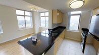 This well-appointed single-floor residence offers a seamless blend of modern design and functional living. The open-concept layout connects the kitchen and living areas, creating an inviting, airy atmosphere throughout. Large, multi-pane windows wrap the space in natural light while framing elevated views of the surrounding cityscape, enhancing the sense of openness.

The kitchen is a standout feature, showcasing sleek dark granite countertops that extend across both the main counter and a central island, providing ample workspace and a striking visual contrast against the light-toned cabinetry. The warm, honey-finished flat-panel cabinets offer generous storage, while the stainless steel sink and contemporary fixtures add a polished, functional touch. A built-in appliance beneath the island further enhances the kitchen's utility.

The flooring transitions from light ceramic tile in the kitchen to warm hardwood in the living area, grounding each zone with its own distinct character while maintaining a cohesive flow. Neutral wall tones and clean architectural lines contribute to the space's bright, understated elegance. Flush and track lighting complement the abundant daylight, ensuring the interior remains well-lit at any hour. Overall, the space presents a clean, modern aesthetic with thoughtful design details throughout.