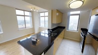 This well-appointed single-floor residence offers a seamless blend of modern design and functional living. The open-concept layout connects the kitchen and living areas, creating an inviting, airy atmosphere throughout. Large, multi-pane windows wrap the space in natural light while framing elevated views of the surrounding cityscape, enhancing the sense of openness.

The kitchen is a standout feature, showcasing sleek dark granite countertops that extend across both the main counter and a central island, providing ample workspace and a striking visual contrast against the light-toned cabinetry. The warm, honey-finished flat-panel cabinets offer generous storage, while the stainless steel sink and contemporary fixtures add a polished, functional touch. A built-in appliance beneath the island further enhances the kitchen's utility.

The flooring transitions from light ceramic tile in the kitchen to warm hardwood in the living area, grounding each zone with its own distinct character while maintaining a cohesive flow. Neutral wall tones and clean architectural lines contribute to the space's bright, understated elegance. Flush and track lighting complement the abundant daylight, ensuring the interior remains well-lit at any hour. Overall, the space presents a clean, modern aesthetic with thoughtful design details throughout.