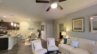 Located at 3202 W Nine Mile Rd. in Pensacola, Florida, this single-floor residence offers a thoughtfully designed open-concept layout that seamlessly connects the main living areas. Crown molding runs throughout the space, adding a refined architectural touch to the interior.

The living area is warm and inviting, featuring dark hardwood-style flooring, a ceiling fan with a light fixture, and ample room for comfortable seating arrangements. The space flows naturally into the dining area, which is illuminated by a modern track lighting fixture overhead, creating a well-lit setting for gatherings.

The kitchen is a standout feature of the home, equipped with dark espresso cabinetry, granite countertops, and stainless steel appliances including a refrigerator, microwave, and range. A breakfast bar with pendant lighting provides additional seating and serves as a functional divide between the kitchen and dining area, making it ideal for both casual meals and entertaining.

Neutral, muted tones on the walls complement the darker flooring and cabinetry throughout, creating a cohesive and contemporary aesthetic. The open sightlines between rooms enhance the sense of space and allow natural light to filter through the interior. Overall, this residence combines practical design with modern finishes for comfortable everyday living.