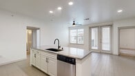 This well-appointed 2-bedroom, 2-bathroom single-story unit offers a thoughtfully designed open-concept layout that maximizes functionality and comfort. The combined kitchen and living area serves as the heart of the home, featuring light wood-look tile flooring, recessed lighting, and a ceiling fan. The kitchen is highlighted by white shaker cabinetry, granite countertops, a center island with an undermount sink and matte black faucet, and a full suite of stainless steel appliances including a French door refrigerator, range, over-the-range microwave, and dishwasher. A stacked washer and dryer unit is conveniently housed within the kitchen area. The living room is bright and airy, with large windows and French doors that provide outdoor access and fill the space with natural light. Both bedrooms are carpeted and equipped with ceiling fans, with the primary bedroom featuring an en-suite bathroom and walk-in closet outfitted with wire shelving. The primary bath includes a glass-enclosed walk-in shower with tile surround. A second full bathroom serves the additional bedroom. Two closets provide ample storage throughout the unit, and a hallway connects the private sleeping quarters to the main living area.
