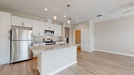 Located at 3180 Shoreline Dr in Largo, Florida, this modern two-story home offers a well-designed layout with contemporary finishes throughout. The main level features an open-concept kitchen that serves as the centerpiece, showcasing white shaker cabinetry, granite countertops, a large central island with pendant lighting, and a full suite of stainless steel appliances. Light wood-style flooring extends across the main living areas, creating a bright and cohesive feel. A staircase with a sleek dark handrail connects the two floors, complemented by a clean hallway with recessed lighting and light hardwood-style flooring. The upper level features carpeted bedrooms that offer natural light through window blinds, providing comfortable and quiet retreats. A walk-in closet with wire shelving adds practical storage to the bedroom suite. The bathroom is finished with granite-topped white vanity cabinetry, a tiled tub-shower combination, and matching wood-look flooring. An attached two-car garage with an automatic opener rounds out the functional amenities of this well-appointed home. The overall aesthetic throughout is clean, neutral, and move-in ready.
