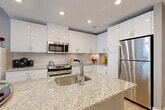Located in Washington, DC's Capitol Riverfront neighborhood, Unit 308 at 1111 New Jersey Ave SE is a thoughtfully designed one-bedroom, one-bathroom residence offering a contemporary urban lifestyle. Light hardwood-style flooring flows throughout the open-plan layout, connecting the living, dining, and kitchen areas seamlessly.

The modern kitchen is a standout feature, boasting high-gloss white cabinetry, granite countertops, a large center island with an undermount sink, subway tile backsplash, and a full suite of stainless steel appliances. The adjacent dining area provides a natural gathering space, while the living room impresses with floor-to-ceiling windows that flood the room with natural light and frame views of the surrounding cityscape.

The spacious bedroom offers a comfortable retreat with plush carpeting and ample closet space — three closets in total are distributed throughout the unit, providing generous storage. The full bathroom features tile flooring, a combined tub and shower, and clean, modern finishes. An in-unit laundry area adds everyday convenience.

Step outside onto the private balcony with glass-railed views overlooking the streetscape and neighboring buildings — an ideal spot to enjoy the vibrant DC surroundings. Recessed lighting throughout completes this polished, move-in-ready urban home.