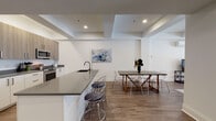 Located at 2–16 High Street in the heart of New Haven, Connecticut, this single-floor unit offers a thoughtfully designed interior with a clean, contemporary aesthetic throughout. Wide-plank wood-look flooring flows continuously across the living areas and bedrooms, providing a cohesive and warm foundation that contrasts with the crisp white walls and recessed lighting overhead.

The open-concept kitchen and dining area serves as a central hub of the space. The kitchen features stainless steel appliances, including a range and built-in microwave, complemented by two-tone cabinetry in white and warm wood tones, and a generous island with a dark quartz countertop and seating for multiple guests. The adjacent dining area offers ample room for a full dining table.

Multiple bedrooms provide comfortable retreats, each featuring hardwood-style flooring, recessed lighting, and large windows that invite natural light. The primary bedroom is notably spacious, with room for a sitting area and access to exterior views. The bathroom is finished with large-format tile flooring, a wood-toned vanity with granite countertop, and a glass-enclosed shower.

A dedicated laundry area includes a full-size washer, matching cabinetry above, and a folding counter. A separate living or flex room with a wall-mounted AC unit and street-facing window adds versatile functionality to this well-appointed unit.