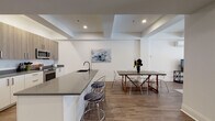 Located at 2–16 High Street in the heart of New Haven, Connecticut, this single-floor unit offers a thoughtfully designed interior with a clean, contemporary aesthetic throughout. Wide-plank wood-look flooring flows continuously across the living areas and bedrooms, providing a cohesive and warm foundation that contrasts with the crisp white walls and recessed lighting overhead.

The open-concept kitchen and dining area serves as a central hub of the space. The kitchen features stainless steel appliances, including a range and built-in microwave, complemented by two-tone cabinetry in white and warm wood tones, and a generous island with a dark quartz countertop and seating for multiple guests. The adjacent dining area offers ample room for a full dining table.

Multiple bedrooms provide comfortable retreats, each featuring hardwood-style flooring, recessed lighting, and large windows that invite natural light. The primary bedroom is notably spacious, with room for a sitting area and access to exterior views. The bathroom is finished with large-format tile flooring, a wood-toned vanity with granite countertop, and a glass-enclosed shower.

A dedicated laundry area includes a full-size washer, matching cabinetry above, and a folding counter. A separate living or flex room with a wall-mounted AC unit and street-facing window adds versatile functionality to this well-appointed unit.