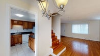This three-bedroom, one-and-a-half-bathroom home spans three floors, offering a well-organized layout with distinct living zones across each level. The main living area features warm hardwood flooring that lends a welcoming character to the space, complemented by neutral wall tones that create a bright and airy atmosphere. Natural light filters in through sizable windows dressed with vertical blinds, enhancing the open feel of the living area. A decorative chandelier anchors the dining or entryway space, adding a touch of classic elegance. A central staircase with rich wood treads connects the floors, serving as both a functional and visual focal point. The kitchen is outfitted with warm wood cabinetry, dark countertops, and tile flooring, providing ample storage and a practical workspace. White appliances complete the kitchen's clean, traditional aesthetic. The transition between the kitchen and living areas is seamless, supporting an efficient and comfortable flow throughout the home. Across its three floors, this residence provides generous room for everyday living, sleeping quarters, and additional flexible space, making it a well-rounded home suited for a variety of lifestyles.