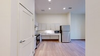 This ADA-compliant two-bedroom, one-bathroom unit in Detroit, Michigan offers a thoughtfully designed layout built with accessibility at its core. Light wood flooring runs throughout the space, creating a bright, cohesive aesthetic across every room. The open kitchen is well-appointed with white shaker-style cabinetry, marble-look countertops, stainless steel appliances including a gas range and full-size refrigerator, and an accessibility-friendly sink and counter configuration featuring knee clearance below. Recessed lighting illuminates the kitchen and living area, enhancing the clean, modern atmosphere. Both bedrooms are comfortably sized with neutral walls and natural light provided by large windows fitted with horizontal blinds. The primary bedroom includes a double-door closet, offering ample storage. The second bedroom is bright and versatile, with an open, airy feel. The bathroom is designed to ADA standards, featuring a roll-in shower with grab bars, a fold-down shower bench, a hand-held showerhead, and an open-access sink with clearance for wheelchair use. The overall design emphasizes functionality, accessibility, and a clean modern aesthetic throughout.