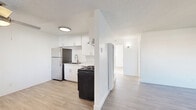 Located at 1241 East Madison Avenue in El Cajon, CA, this two-bedroom, one-bathroom residence offers a clean, modern aesthetic across its single-floor layout. Light wood-style flooring runs throughout the space, complementing the bright white walls and textured ceilings to create a cohesive, airy feel.

The combined kitchen and living room area serves as the heart of the home. The kitchen is well-appointed with white shaker-style cabinetry, light stone-look countertops, a stainless steel refrigerator, a gas range, and an under-cabinet range hood — all positioned to maximize functionality. The open living room area features large windows with vertical blinds that invite abundant natural light, along with a wall-mounted heater and a decorative pendant light fixture near the entryway.

Both bedrooms are comfortably scaled, filled with natural light from barred windows that frame outdoor views of palm trees and the surrounding neighborhood. Each room features the same light flooring and clean white walls. The primary bedroom includes a full-width sliding closet, while a second closet provides additional storage elsewhere in the unit.

The bathroom is finished in an all-white palette, featuring a tub-shower combination with tile surround, a brushed nickel curved shower rod, a marble-top vanity, and wood-style tile flooring for a polished, consistent look.