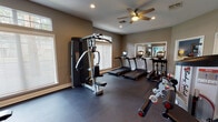 This single-level fitness space is thoughtfully designed to support a wide range of workout routines. The room features neutral taupe walls, recessed lighting, and ceiling fans that contribute to a comfortable and functional exercise environment. Rubber flooring covers the entire area, providing both durability and safety underfoot.

Natural light enters generously through multiple large windows fitted with white horizontal blinds, including transom windows positioned above the main panes. These windows are distributed across several walls, ensuring the space feels bright and open. Strategic placement of large wall-mounted mirrors further amplifies the sense of space and allows users to monitor their form during exercise.

The cardio zone is well-appointed with multiple treadmills and an elliptical trainer, each equipped with individual monitors. Strength training is supported by a multi-function cable machine, a dedicated free-weight rack stocked with a full set of dumbbells, a weight bench, and additional resistance equipment including a rowing-style machine and stationary bike.

The overall layout is organized to allow clear movement between equipment zones. Ventilation is supported by ceiling fans positioned throughout the room, and informational signage is posted on the walls, reinforcing the space's professional fitness-center character.