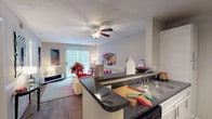 This single-floor residence offers a thoughtfully designed layout that balances comfort and functionality throughout. The open-concept kitchen flows seamlessly into the living area, creating an inviting, connected space ideal for everyday living. The kitchen is equipped with dark granite countertops, white cabinetry, a double-basin sink, black appliances including a refrigerator and gas range, and wood-look flooring that extends through the common areas. Track lighting overhead adds a practical, modern touch. A breakfast bar with additional counter space bridges the kitchen to the living room, which features hardwood-style floors, a ceiling fan, and sliding glass doors that allow natural light to fill the space. Each bedroom is carpeted for comfort and fitted with a ceiling fan. The primary bedroom is notably spacious, complete with a walk-in closet and a private en-suite bathroom featuring a tub-shower combination. Additional bedrooms are well-proportioned, each with ample natural light from sizable windows and convenient access to a full bathroom. Both bathrooms include tub-shower combinations and granite-topped vanities. Neutral tones throughout the home create a clean, cohesive ambiance that is both versatile and welcoming.