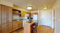 Located at 1706 Fairway Drive in Walla Walla, Washington, this single-floor residence offers a thoughtfully designed layout that balances comfort and functionality. The kitchen is a standout feature, outfitted with warm honey-toned wood cabinetry, ample counter space, a double-basin sink, white appliances including a refrigerator, electric range, built-in microwave, and dishwasher. A central island with a breakfast bar and bar seating adds both workspace and casual dining convenience. Light hardwood-style flooring flows throughout the kitchen and connecting areas. The living room is carpeted and bathed in natural light, courtesy of a sliding glass door that opens to a private balcony with outdoor views — an inviting space for relaxation. The bedroom is generously sized, featuring plush carpeting, large windows that bring in abundant natural light and scenic exterior views, and tray ceiling detailing that adds architectural character. The bathroom includes a wood-toned vanity with a single sink, hardwood-style flooring, and a shower-tub combination. Throughout the residence, a warm, neutral color palette and consistent use of natural wood tones create a cohesive and welcoming ambiance.