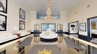 Located at 45 Creekside Lane in Malvern, PA, this expansive single-floor space offers a sophisticated and meticulously designed interior that commands attention from the moment of entry. The grand entrance foyer welcomes visitors with soaring ceilings, floor-to-ceiling arched windows draped in sheer white curtains, and highly polished black tile flooring that reflects the abundant natural light pouring in from the street-facing facade.

At the heart of the space lies a stunning central lobby anchored by a dramatic multi-tiered crystal chandelier suspended from a double-height ceiling. A circular white lounge piece serves as a central focal point, flanked by decorative gold-accented panel screens and illuminated base moldings that lend a luxurious ambiance. A gold heraldic crest emblem is featured prominently in the flooring, reinforcing the space's upscale character.

Beyond the lobby, the open lounge and gathering area features rich hardwood flooring, a linear fireplace set against wood-paneled walls, and a bank of grand arched windows offering sweeping outdoor views. Track lighting and soaring ceilings amplify the sense of openness. Additional corridors are finished with polished dark tile, elegant console furnishings, and framed artwork, connecting seamlessly to private rooms with refined, boutique-style interiors. Throughout, the design balances bold architectural details with a refined, welcoming atmosphere.