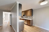 Located at Antoinette Lane in South San Francisco, this 2-bedroom, 1-bathroom residence offers a thoughtfully designed single-floor layout. The living room welcomes you with a paneled front door, a wide picture window fitted with blinds that fills the space with natural light, and warm wood-look flooring complemented by crown molding throughout.

The open kitchen is a standout feature, showcasing two-tone wood-grain cabinetry in rich walnut and dark finishes, a textured tile backsplash, white quartz countertops, a stainless steel sink, and stainless steel appliances including a refrigerator and dishwasher. A peninsula with matching cabinetry defines the boundary between the kitchen and living areas, while recessed lighting adds a polished touch.

Both bedrooms are carpeted and finished in neutral tones, offering a calm and comfortable retreat. The primary bedroom provides a generous footprint with a closet, while the second bedroom features a window with views of the surrounding community. A hallway connects the main living spaces to the bedrooms and bathroom.

The bathroom is clean and functional, featuring a tiled tub-shower combination, a wood-grain vanity with a white countertop, and a mirrored medicine cabinet. Throughout the home, consistent neutral paint tones and modern finishes create a cohesive, contemporary aesthetic.