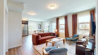 This thoughtfully designed 2-bedroom, 2-bathroom residence offers a comfortable and functional single-floor layout with warm hardwood flooring connecting each space seamlessly. Entry is made through a welcoming hallway accented by louvered doors and decorative touches, leading into an open and airy living area filled with natural light from multiple windows dressed in warm-toned curtains. The living space flows naturally into a bright dining area surrounded by large windows offering pleasant outdoor views, creating an ideal setting for everyday dining. The kitchen is well-equipped with two-tone cabinetry — white uppers paired with dark lower cabinets — complemented by a tile backsplash, stone countertops, and stainless steel appliances including a full-size refrigerator, dishwasher, and range. The primary bedroom is generously sized, featuring a large window and walk-in closet with built-in hanging storage. The second bedroom offers a distinctive arched window, adding architectural character. Both bathrooms are cleanly finished; one features a glass-enclosed soaking tub and classic black-and-white hexagonal tile flooring. The unit is completed by a dedicated closet for additional storage, making this residence both practical and refined throughout.