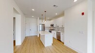 This well-appointed 3-bedroom, 2-bathroom unit at 518 Vosseller Ave in Bound Brook, NJ offers a thoughtfully designed, single-floor layout with a clean, modern aesthetic. The open-concept kitchen and living area serves as the heart of the home, featuring a sleek center island with quartz countertops, white shaker cabinetry with gold hardware, a subway tile backsplash, and a full suite of stainless steel appliances. Stylish gold pendant lights hang above the island, complementing the recessed lighting throughout. Light hardwood flooring flows seamlessly across the entire unit, enhancing its bright and airy feel. Large windows in the living area and bedrooms invite abundant natural light and offer views of the surrounding neighborhood. The spacious primary bedroom includes a well-organized walk-in closet with built-in shelving and hanging rods. Both bathrooms are finished with neutral tile flooring and clean white vanities; the primary bath features a double-sink vanity with brushed black hardware and a large mirror. A dedicated utility room houses in-unit laundry and mechanical systems for added convenience. The overall ambiance is fresh, modern, and move-in ready, ideal for comfortable everyday living.