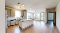 This thoughtfully designed one-bedroom, one-bathroom unit offers a bright and functional open-concept layout that seamlessly connects the kitchen and living area. Light wood-look flooring runs throughout, lending a clean and cohesive aesthetic across every room.

The kitchen is a standout feature, boasting a central granite-topped island, crisp grey shaker cabinetry, a white tile backsplash, and a full suite of stainless steel appliances including a refrigerator with ice maker, range, microwave, and dishwasher. Track lighting illuminates the space, while a window over the sink brings in natural light.

The living area is open and airy, benefiting from multiple large windows and a ceiling fan that enhance both comfort and brightness. A glass door provides access to the exterior, furthering the sense of openness.

The bedroom is a comfortable and well-lit retreat, featuring a ceiling fan, a sizable window with outdoor views of lush greenery, and generous proportions. The full bathroom is elegantly finished with a granite-topped vanity, a soaking tub, a separate glass-enclosed shower, and wood-look tile flooring, with an adjacent walk-in closet offering ample storage.

Completing the unit is a dedicated laundry room with a full-size washer and dryer and overhead shelving for added convenience.