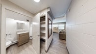 Located at 331 North Ottawa Street in Joliet, Illinois, this efficiently designed one-bedroom, one-bathroom unit makes excellent use of its compact footprint. The open-concept main area seamlessly combines the living and sleeping spaces, with light wood-look flooring running throughout and large windows fitted with horizontal blinds that allow natural light to fill the room. The living area features a wall-mounted flat-screen television set against a wood-paneled accent wall, complemented by a sofa and a marble-top coffee table.

The kitchen is thoughtfully outfitted with white shaker-style cabinetry, granite countertops, a subway tile backsplash, stainless steel appliances including a full-size refrigerator, and a double-basin sink — providing full cooking functionality within a streamlined galley layout. A small dining area sits adjacent to the kitchen.

A built-in open shelving unit in the hallway offers convenient storage, while a decorative framed mirror adds visual depth to the transitional space. The bathroom is clean and modern, featuring a wood-toned vanity with granite countertop, an undermount sink, a large backlit mirror, and a tiled shower. The white block masonry walls visible in portions of the unit lend an industrial character to the otherwise contemporary interior design.