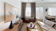 This well-appointed single-floor residence offers a cohesive blend of modern and organic design elements throughout its thoughtfully laid-out spaces. The living room is bright and welcoming, featuring a ceiling fan, large windows with patterned drapes, and a sliding glass door that allows natural light to fill the room. The space is anchored by a neutral palette, complemented by warm wood tones and layered textures. The kitchen is equipped with stainless steel appliances, including a range, built-in microwave, dishwasher, and a side-by-side refrigerator. Rich wood-toned cabinetry extends to the ceiling, offering ample storage, while clean white countertops provide generous prep space. A cozy dining nook with a round table sits adjacent, bathed in natural light from large windows. The primary bedroom is serene and spacious, featuring soft carpet, elegant bedside lighting, and a bold decorative wall piece as a focal point. A secondary bedroom offers a bright, airy atmosphere with natural light and tasteful artwork. The bathroom includes a dual-sink vanity with wood cabinetry, a tub-shower combination, and a window for natural light. A dedicated office area with a herringbone-patterned area rug and built-in desk completes this versatile and inviting home.