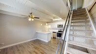 Located at 985 Grand Canyon Parkway in Hoffman Estates, IL, this two-floor unit offers a well-designed layout spread across two levels. The main floor features an open-concept kitchen and living area, highlighted by striking exposed beam ceilings with white shiplap detailing that add architectural character throughout. The kitchen is a standout, boasting crisp white shaker cabinetry, a mosaic tile backsplash, stainless steel appliances including a range, built-in microwave, dishwasher, and refrigerator, as well as a generous island with a white quartz countertop and pendant lighting overhead. White-painted brick accent walls add a distinct industrial-chic charm. The living area features durable wood-look flooring, a ceiling fan, and windows that invite natural light while offering views of the outdoors. A staircase with a modern metal railing leads to the upper level, which provides additional living space. A hallway and bathroom round out the interior. Outside, a private patio area enclosed by fencing offers a personal outdoor retreat. The overall ambiance is bright, clean, and modern with thoughtful design details throughout.