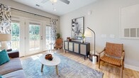 This contemporary 820 square foot apartment offers a thoughtfully designed living space with two bedrooms and two bathrooms. The heart of the home is an open-concept living area, seamlessly connecting the kitchen, dining, and living spaces. The kitchen boasts crisp white cabinetry, stainless steel appliances, and a functional island with seating, perfect for casual dining or entertaining.

Natural light floods the space through large windows, enhancing the airy feel of the home. The living room features a comfortable gray sofa, accented with colorful pillows, and unique oval mirrors that add depth to the space. Hardwood floors run throughout, lending warmth and continuity.

The primary bedroom, measuring 140 square feet, is a serene retreat with a large window offering outdoor views. Both bedrooms are well-appointed with modern furnishings and ample natural light. The bathrooms are stylishly designed with clean lines and contemporary fixtures.

Thoughtful details like pendant lighting, artistic wall decor, and strategically placed plants contribute to the overall modern aesthetic. The apartment also offers outdoor access, likely through a balcony or patio, extending the living space and providing a connection to the surrounding environment.