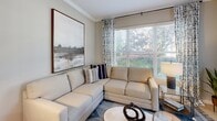 This single-floor residence located in Charlotte, NC, offers a thoughtfully designed layout that balances comfort and functionality. The living room is bathed in natural light streaming through large windows dressed with elegant blinds and patterned curtains, complemented by crown molding and neutral tones that create a warm, inviting atmosphere. Adjacent to the living area, the dining space features light hardwood-style flooring, a classic chair rail detail, and pendant lighting that adds a contemporary touch, with an open sightline connecting seamlessly to the kitchen. The kitchen is outfitted with warm wood cabinetry, granite-style countertops, stainless steel appliances including a refrigerator, range, microwave, and dishwasher, along with a built-in desk area ideal for a home office setup. Two well-proportioned bedrooms feature plush carpeting, generous windows with ample natural light, and soft neutral wall tones. Each bedroom is served by its own bathroom; one bath includes a glass-enclosed shower with a granite-topped vanity and wood cabinetry, while the second offers a tub/shower combination with a matching vanity. Light hardwood-style flooring flows throughout the main living areas, tying the space together with a clean, cohesive aesthetic.