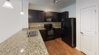 This single-floor residence offers a thoughtfully designed layout with a cohesive blend of comfort and functionality. The kitchen stands out as a centerpiece, showcasing rich dark cabinetry, granite countertops with a stainless steel sink, a tile backsplash, and black appliances including a range, over-the-range microwave, and refrigerator. Wood-style flooring and crown molding add a refined touch, while track lighting and a pendant light enhance the space. The bedrooms feature plush wall-to-wall carpeting and ceiling fans, with natural light filtering through blinds-covered windows. One bedroom includes direct access to a spacious walk-in closet, providing generous storage. The bathroom is cleanly appointed with a tub and shower combination, a curved shower rod, brushed nickel grab bar and fixtures, and neutral tile flooring. A dedicated laundry area accommodates a full-size side-by-side washer and dryer with wire shelving above for additional storage. Throughout the residence, neutral wall tones and clean white trim create a bright, welcoming ambiance. The overall floor plan, as seen in the 3D model, reveals a well-organized and efficiently connected layout ideal for comfortable everyday living.