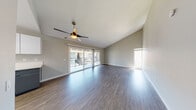 This single-floor residence offers a clean, contemporary design throughout. The living area is a standout space, featuring vaulted ceilings, wood-style flooring in a rich gray-brown tone, and a ceiling fan with a built-in light fixture. Large sliding glass doors flood the room with natural light and open to a private balcony, offering views of the surrounding exterior. A secondary window further enhances the bright, airy atmosphere.

The kitchen is well-appointed with a two-tone design, pairing white upper cabinetry with slate-gray lower cabinets and crisp white countertops. Stainless steel appliances, including a range, microwave, and dishwasher, provide a modern touch, while a window above the sink brings in additional natural light. Light wood-style flooring completes the functional layout.

The bedrooms continue the wood-style flooring theme and each includes a ceiling fan, natural light from windows with blinds, and sliding mirrored closet doors offering generous storage. One bedroom features notably elevated ceilings, adding to the sense of space.

The two bathrooms are finished with gray cabinetry and white countertops. One includes a walk-in shower, while the other features a shower-tub combination, both with brushed nickel fixtures.