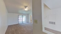 This single-floor residence offers a well-organized layout designed for comfortable everyday living. The main living area is generously sized, featuring wall-to-wall carpeting, a ceiling fan with integrated lighting, and sliding glass doors that open to a private balcony, filling the space with natural light. A structural column adds architectural definition to the open floor plan, which connects seamlessly to additional rooms. The kitchen is efficiently designed with a galley-style layout, featuring warm wood-toned cabinetry, white countertops, hardwood-style flooring, and a full suite of black appliances including a refrigerator, electric range, and over-the-range microwave. The bedrooms are carpeted and bright, each equipped with a ceiling fan and windows fitted with blinds for light control and privacy. One bedroom features direct access to a bathroom vanity area with warm wood cabinetry and a large mirror with Hollywood-style lighting. Both bathrooms include full tub-shower combinations with clean white surrounds. Throughout the unit, a neutral white color palette creates a bright, airy ambiance, while consistent carpeting in the living and sleeping areas ties the space together cohesively.