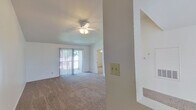 This single-floor residence offers a well-organized layout designed for comfortable everyday living. The main living area is generously sized, featuring wall-to-wall carpeting, a ceiling fan with integrated lighting, and sliding glass doors that open to a private balcony, filling the space with natural light. A structural column adds architectural definition to the open floor plan, which connects seamlessly to additional rooms. The kitchen is efficiently designed with a galley-style layout, featuring warm wood-toned cabinetry, white countertops, hardwood-style flooring, and a full suite of black appliances including a refrigerator, electric range, and over-the-range microwave. The bedrooms are carpeted and bright, each equipped with a ceiling fan and windows fitted with blinds for light control and privacy. One bedroom features direct access to a bathroom vanity area with warm wood cabinetry and a large mirror with Hollywood-style lighting. Both bathrooms include full tub-shower combinations with clean white surrounds. Throughout the unit, a neutral white color palette creates a bright, airy ambiance, while consistent carpeting in the living and sleeping areas ties the space together cohesively.