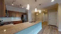 Located at 14201 Kanis Rd in Little Rock, Arkansas, this single-floor residence offers a thoughtfully designed open-concept layout with modern finishes throughout. The kitchen serves as a central hub of the space, showcasing warm medium-toned wood cabinetry, a classic white subway tile backsplash, granite countertops, and a full suite of stainless steel appliances including a refrigerator, range, and built-in microwave. A spacious peninsula with an undermount sink and pendant lighting above provides ample counter space and connects seamlessly to the living area. Track lighting and crown molding add refined detail to the kitchen ceiling. The open living area features durable wood-look flooring, a ceiling fan, and natural light from blinds-fitted windows. Bedrooms are carpeted for comfort, each equipped with a ceiling fan and a built-in closet with shelving. Natural light filters in through windows with blinds. The bathrooms feature wood-look tile flooring, granite-topped vanities, and rich wood cabinetry. One bathroom offers a soaking tub with large-format tile surround, while another provides a standard tub-shower combo. Crown molding and neutral tones create a cohesive, clean aesthetic throughout the entire space.