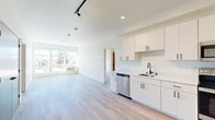 This thoughtfully designed 2-bedroom, 3-bathroom residence at 2002 N Monroe St in Spokane, Washington offers a clean, modern aesthetic throughout. The open-concept living and kitchen area is anchored by light hardwood-style flooring, crisp white walls, and large windows that flood the space with natural light and frame views of the surrounding Spokane neighborhood. The contemporary kitchen is well-appointed with white shaker-style cabinetry featuring black hardware, stainless steel appliances including a refrigerator, range, microwave, and dishwasher, along with a undermount sink and ample counter space. Track and recessed lighting add a polished finishing touch. The living area is bright and spacious, benefiting from a large window bank that opens up the room. Both bedrooms are comfortably sized, each with large windows offering neighborhood views and light-toned flooring. The primary bedroom includes a dedicated walk-in closet outfitted with wire shelving for organized storage. Three full bathrooms are finished in a consistent modern style, featuring white vanities, black fixtures, round mirrors, and tub/shower combinations. An in-unit stacked washer and dryer adds everyday convenience to this well-appointed Spokane residence.