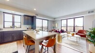 This single-floor residence showcases a thoughtfully designed open-concept layout where the kitchen, dining, and living areas flow seamlessly together. The kitchen is a standout feature, equipped with dark shaker-style cabinetry, stainless steel appliances including a French door refrigerator and built-in oven, a white quartz island with bar seating, and a white subway tile backsplash. Large windows and balcony access fill the kitchen and adjoining spaces with abundant natural light.

The living area is generously proportioned, anchored by oversized windows that frame outdoor views and invite natural light throughout the day. Light wood-tone flooring runs throughout the main living spaces, complementing the contemporary aesthetic.

The primary bathroom features a dual-sink vanity with white quartz countertops and dark cabinetry, a glass-enclosed shower, and direct access to a walk-in closet. A secondary bathroom offers a soaking tub with shower combination and matching dark cabinetry.

Each bedroom is well-sized, benefiting from large windows with outdoor views. The primary bedroom includes a ceiling fan and access to the en-suite bath. Overall, the space presents a modern, cohesive design with upscale finishes throughout.