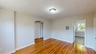 Located at 50 W Maple Ave in Merchantville, NJ, this two-bedroom, one-bathroom unit offers a thoughtfully arranged single-floor layout. Warm-toned hardwood flooring runs throughout the living areas, bedrooms, and hallway, lending a sense of continuity and character to the space. The living room is bright and open, highlighted by a distinctive arched doorway that leads into the hallway, adding an architectural touch to the otherwise clean, neutral interior. Natural light filters in through multiple windows, with pleasant views of mature trees outside. The primary bedroom is a comfortable size and benefits from natural light and a baseboard heating unit, while the second bedroom offers a cozy, versatile space with its own hardwood floors and neutral walls. The kitchen features light flooring, a window overlooking the greenery outside, and includes a range. A connecting hallway provides access to the full bathroom, which is finished with classic white subway tile surrounding a soaking tub and a frosted window for privacy and natural light. The unit's clean white walls, consistent hardwood floors, and efficient layout make it a practical and inviting space in a residential Merchantville neighborhood.