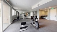 This fitness center is a thoughtfully designed, single-floor facility that offers a complete workout environment for users of all fitness levels. The space is finished with durable dark carpeted flooring throughout, providing a comfortable surface for exercise, while soft sage-green walls and recessed lighting create a clean, modern aesthetic.

The main workout area is generously proportioned, providing ample room to move freely between equipment stations. Floor-to-ceiling mirrors line key sections of the walls, enhancing the sense of openness and allowing users to monitor their form during training. A large sliding glass door floods one end of the space with natural light and offers views of an outdoor courtyard, adding an airy, welcoming atmosphere.

The facility is well-stocked with a diverse selection of equipment. Cardio machines include a Spirit treadmill, a recumbent bike, and an elliptical trainer. Strength training options feature a cable machine with multiple attachment points, a multi-station weight machine, a dedicated dumbbell rack with a full range of free weights, and an adjustable workout bench. A separate alcove within the space provides an additional, more private area for focused training.

Restroom facilities are conveniently accessible on-site, and the space is served by clearly marked emergency exits, ensuring safety and convenience for all users.