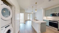 Located at 7051 Stacy Rd in McKinney, TX, this 1-bedroom, 1-bathroom unit offers a thoughtfully designed layout that maximizes every square foot. The open-concept living area features warm wood-look luxury vinyl plank flooring, a ceiling fan, and French doors that lead to a private balcony, filling the space with natural light and outdoor views of the surrounding community.

The kitchen is a standout feature, showcasing sage-green shaker cabinetry that reaches to the ceiling, a white quartz waterfall island with an undermount sink and gold-toned faucet, stainless steel appliances including a refrigerator, electric range, and microwave, and a classic subway tile backsplash. Gold pendant lights above the island add a refined touch. A stacked in-unit washer and dryer is conveniently tucked nearby.

The generously sized bedroom features plush carpet, a ceiling fan, and a large window with exterior views. It connects directly to the full bathroom, which includes sage-green cabinetry with brushed gold hardware, a white quartz countertop, wood-look flooring, and a framed mirror. A dedicated walk-in closet with built-in shelving and dual hanging rods provides ample storage, completing this well-finished unit.