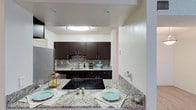 This single-floor 1-bedroom, 1-bathroom residence offers a thoughtfully designed layout that maximizes both comfort and functionality. The kitchen serves as a standout feature, showcasing rich dark espresso cabinetry that provides ample storage, complemented by striking granite countertops with a classic veining pattern. A mosaic tile backsplash adds texture and visual interest between the counters and upper cabinets, tying the design together with a contemporary flair. The kitchen is equipped with a smooth-top electric cooktop seamlessly integrated into the granite surface, a stainless steel refrigerator, and recessed lighting overhead that ensures the space is well-lit. A breakfast bar extension of the granite countertop creates a casual dining area, offering additional seating and a natural gathering spot. The open sightlines between the kitchen and adjoining areas contribute to an airy, connected feel throughout the home. Neutral wall tones provide a clean, versatile backdrop that complements the darker cabinetry and light stone surfaces. The overall ambiance of the residence is modern and inviting, with quality finishes that reflect careful attention to detail in every corner of this efficiently designed single-level home.