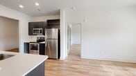 Located at 207 Gresham Ln in Mooresville, NC, this single-floor residence offers a clean, contemporary design highlighted by light wood-tone flooring and crisp white walls throughout. The open-concept layout connects the kitchen, dining, and living areas seamlessly, creating a spacious and airy feel.

The kitchen is well-appointed with dark cabinetry, stainless steel appliances including a refrigerator, range, and microwave, white countertops, and a tile backsplash. A built-in wine rack adds a functional decorative touch. A peninsula with a sink and pendant lighting overhead bridges the kitchen to the living area, which features a ceiling fan with light and multiple windows that invite generous natural light.

Adjacent to the main living space is a bright dining area near a glass-panel exterior door flanked by windows, providing outdoor views and additional sunlight. The bedrooms are well-sized, each featuring wood-tone flooring, ceiling fans, and windows with blinds. The bathroom includes wood-tone flooring and connects conveniently to an in-unit laundry area with washer and dryer. The overall ambiance is modern, clean, and move-in ready.