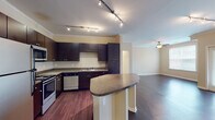 This single-floor residence offers a thoughtfully designed layout that balances functionality and comfort. The open-concept kitchen is a standout feature, showcasing rich dark cabinetry that extends to the ceiling, granite-style countertops, and a full suite of stainless steel appliances including a refrigerator, range, microwave, and dishwasher. A curved breakfast bar peninsula provides additional counter space and serves as a natural divider between the kitchen and the adjoining living area. Track lighting illuminates the kitchen, while crown molding adds a refined architectural detail throughout.

The living area is spacious and open, with gleaming dark hardwood floors and elegant French doors that open to an outdoor balcony, allowing natural light to fill the room. A ceiling fan adds to the comfort of the space.

The bedroom features plush carpeting, a ceiling fan, and a generous window that brings in soft natural light. The bathroom is clean and functional, featuring a tub/shower combination, a dark-cabinetry vanity with a granite-style countertop, and stone-patterned tile flooring. The entry hallway leads seamlessly into the main living spaces, creating a smooth and logical flow throughout the residence.