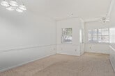 This well-organized one-bedroom, one-bathroom unit is laid out across a single floor, offering a comfortable and efficient use of space. The galley-style kitchen features dark wood cabinetry lining both walls, white countertops, a stainless steel double sink, a stainless steel refrigerator, and an electric range, all set over durable hardwood-style flooring. Adjacent to the kitchen, a hallway connects the main living areas and includes space for an in-unit washer, adding everyday convenience.

The living area is carpeted and bright, with neutral white walls and a ceiling fan with a light fixture overhead. A standout feature is the set of French doors that open to an outdoor area, allowing natural light to fill the room and providing a seamless connection to the exterior. The bedroom is generously proportioned, also carpeted, and equipped with its own ceiling fan. It connects directly to the rest of the unit through a private door and offers a dedicated closet for storage.

The bathroom is clean and functional, featuring a full tub-and-shower combination with white tile surround, a chrome shower rod, and a vanity sink. Two hallways guide circulation throughout the unit, contributing to a logical and easy-to-navigate floor plan. Overall, the space presents a practical and comfortable living environment.