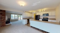 This single-floor residence offers a well-organized layout designed for comfortable everyday living. The open-concept living area is a standout feature, anchored by a full brick accent wall housing a wood-burning fireplace with a classic white mantel. Sliding glass doors flood the room with natural light and provide direct access to a private balcony with outdoor views. Plush neutral carpeting extends throughout the living and bedroom areas, contributing to a warm, cohesive ambiance.

The kitchen is thoughtfully designed with ample white cabinetry, a central island, neutral countertops, and a full suite of black appliances including a refrigerator, range, built-in microwave, and dishwasher. Stone-look tile flooring grounds the space, and track lighting ensures the area is well-illuminated. The kitchen opens directly to the living space, reinforcing the open-plan feel.

The bedrooms offer generous proportions with soft carpeting and closet access. The bathroom features tile flooring, a tub-shower combination, white cabinetry with warm countertops, and clean, bright finishes. A dedicated laundry area with an in-unit washer and a utility space housing a water heater provide added practicality. Overall, the space presents a functional, move-in-ready layout with classic residential character.