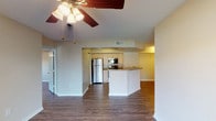 This single-floor residence features a thoughtfully designed open-concept layout connecting the living area and kitchen. The living space is anchored by dark hardwood-style flooring that runs throughout and a ceiling fan with integrated lighting. A large sliding glass door at one end of the living area floods the space with natural light and provides views of the surrounding greenery outside.

The kitchen is positioned centrally and is accessible via a peninsula-style breakfast bar with a dark granite-style countertop. White cabinetry lines the walls, complemented by a full suite of stainless steel appliances, including a refrigerator, range, and over-the-range microwave. A paneled closet provides additional storage adjacent to the kitchen.

Multiple bedrooms carry the same dark hardwood-style flooring and are each equipped with ceiling fans and windows that allow natural light. At least one bedroom features a built-in closet with wire shelving, offering practical storage solutions.

The bathrooms maintain a clean, functional aesthetic with light tile flooring, vanities topped with granite-style counters, and tub-shower combinations. Neutral wall tones and bright overhead lighting create a bright, airy atmosphere throughout the unit.