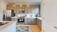 Located on Hilton Head Island, SC, this thoughtfully designed single-floor residence offers a seamless blend of modern finishes and coastal-inspired style. A clean, well-lit entryway hallway with light hardwood-style flooring and crisp white panel doors sets the tone for the interior.

The kitchen is a standout feature, outfitted with sage-gray shaker cabinetry extending to the ceiling, white quartz countertops, a classic subway tile backsplash, and a full suite of stainless steel appliances including a gas range, over-range microwave, and French door refrigerator. A dedicated workspace nook adjacent to the kitchen adds practical versatility.

The open living and dining areas are bathed in natural light from large windows dressed with elegant ombre drapery. The dining space accommodates a full table and offers views to the outdoors, while the living room provides a comfortable, coastal-chic retreat.

The bedrooms are generously sized with plush carpeting, ample closet space including a walk-in closet, ceiling fans, and windows that allow abundant daylight. The primary bathroom impresses with a long dual-sink vanity, gray cabinetry, a glass-enclosed walk-in shower with white tile, and built-in open shelving for storage. Light tile flooring and recessed lighting complete the polished look throughout.