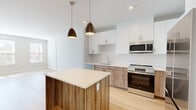 Located at 22 Mount Carmel Way in Worcester, MA, this well-designed 2-bedroom, 1-bathroom residence offers a thoughtful layout across a single floor. Light hardwood flooring runs throughout the space, lending warmth and continuity from room to room.

The kitchen is a standout feature, showcasing a modern two-tone design with crisp white upper cabinets and warm wood-finished lower cabinetry paired with a white quartz countertop island. Stainless steel appliances—including a refrigerator, range, microwave, and dishwasher—complete the contemporary look, while stylish pendant lights hang above the island, adding an inviting ambiance. A subway tile backsplash adds a clean, polished touch.

The living area is open and airy, benefiting from the flowing layout and natural light. The spacious primary bedroom includes generous wall space and ample room for furnishings, while the second bedroom features large windows with outdoor views, filling the room with abundant natural light. Two closets provide practical storage throughout the unit.

The bathroom is clean and modern, featuring a glass-door walk-in shower with light gray subway tile surround and chrome fixtures, complemented by the same hardwood-style flooring. The overall aesthetic throughout is contemporary and neutral, creating a bright, move-in-ready living environment.
