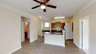 Located at 3801 Glen Verde Trl in Raleigh, NC, this single-floor residence offers a well-designed layout with a comfortable and functional flow throughout. The open-concept kitchen serves as a central hub, featuring warm honey-toned cabinetry, dark laminate countertops, a kitchen island with a sink, stainless steel appliances including an electric range, over-the-range microwave, and refrigerator. Hardwood-style flooring runs through the main living and kitchen areas, adding a clean, modern aesthetic. The spacious living room is accented by crown molding, a ceiling fan, and a large sliding glass door that floods the space with natural light and provides direct access to an outdoor area. The bedrooms are carpeted for comfort, each equipped with ceiling fans and windows that bring in natural light. The primary bedroom includes access to a walk-in closet and an en-suite bathroom. The bathrooms are finished with dark-topped vanities and full tub-shower combinations. Throughout the home, neutral warm tones on the walls create a bright and inviting atmosphere, making this a well-appointed single-story residence.