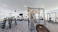 Located at 24 Winnow Walk in Wilmington, NC, this single-story fitness center offers a generously sized, thoughtfully organized space designed to accommodate a wide range of workout styles. The facility is divided into distinct functional areas, all finished with a clean, modern aesthetic characterized by crisp white walls, recessed lighting, and ceiling fans throughout.

The main workout floor is expansive, featuring durable patterned carpet tiles and an impressive array of strength training equipment, including multi-station cable machines, power racks with adjustable benches, and a full dumbbell rack spanning a broad weight range. Large windows line the walls, flooding the space with natural light and providing views of the surrounding greenery.

A dedicated cardio zone houses multiple treadmills, elliptical trainers, and stationary cycling bikes, each equipped with individual screens. Wall-mounted flat-screen televisions are positioned for easy viewing during workouts, and mirrors along certain walls enhance the sense of openness.

A separate studio room provides a bright, open-floor area ideal for stretching, yoga, or functional training. This room features smooth flooring, large windows, TRX suspension straps, and full-length mirrors that maximize the sense of space. The overall ambiance across the facility is bright, airy, and well-ventilated, creating an inviting environment for comprehensive fitness training.