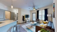 This efficiently designed 3-bedroom, 2-bathroom unit is arranged on a single floor, making thoughtful use of its compact footprint. The open-concept kitchen and living area serves as the central hub of the space. The kitchen is outfitted with dark espresso cabinetry, a blue mosaic tile backsplash, stainless steel appliances, and a white-topped island with an integrated sink and bar seating illuminated by pendant lighting. Light wood-style flooring runs throughout, contributing to a clean, cohesive aesthetic.

The living area features a ceiling fan, a glass door leading to a balcony, and a large adjacent window that draws in ample natural light. The primary bedroom includes a walk-in closet with built-in shelving and a hanging rod, offering functional storage. The additional bedrooms are modestly sized with windows providing natural light. Both bathrooms follow a consistent design, featuring dark vanity cabinetry, granite-style countertops, large framed mirrors, and shower-tub combinations. The neutral color palette and light flooring throughout give the unit a bright, modern character well-suited for efficient, comfortable living.