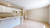 Located at 8742 Orion Ave in the North Hills neighborhood of Los Angeles, CA, this two-bedroom, one-bathroom unit offers a practical and efficient single-floor layout. The open-concept kitchen and dining area serves as the heart of the space, featuring white cabinetry, granite-style countertops, a tile-topped breakfast bar with seating, a gas range, and an under-cabinet range hood — all finished with light ceramic tile flooring that extends throughout the unit. A textured ceiling and warm neutral wall tones lend a clean, understated aesthetic to the main living area, which flows openly from the kitchen peninsula. The two bedrooms are modestly sized, with the primary bedroom offering a window that brings in natural light, complemented by the same tile flooring and neutral palette found throughout the home. A connecting hallway provides access to the shared full bathroom, which includes a tiled shower-tub combination with warm earth-tone wall tiles, a single vanity with white cabinetry, and a small window for ventilation. The layout is straightforward and functional, making efficient use of the available space throughout.